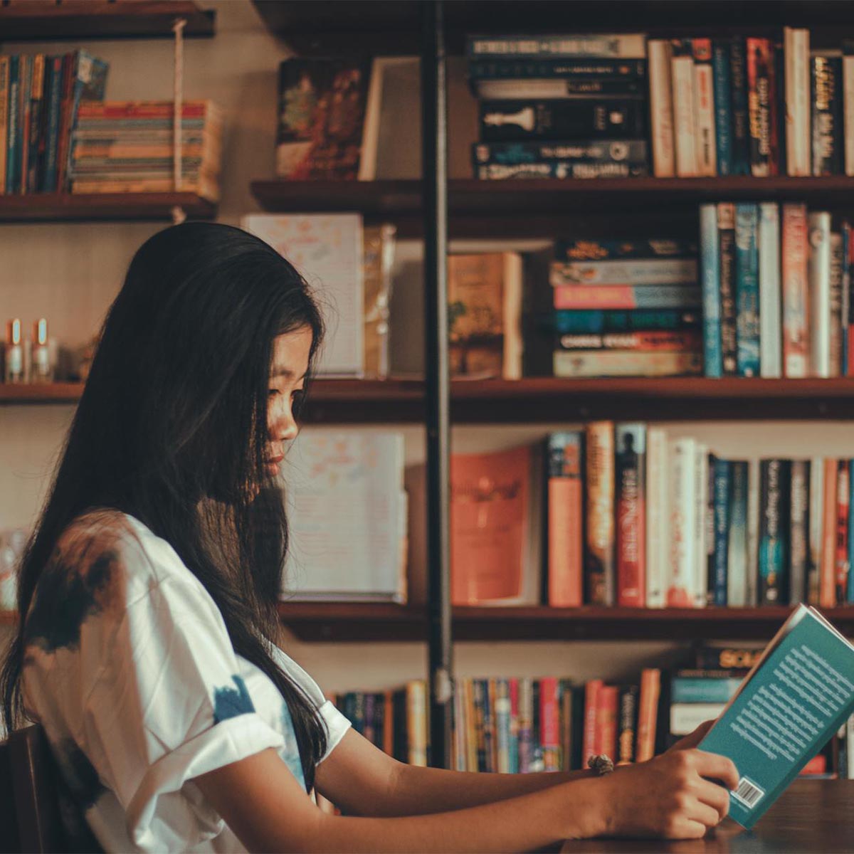 Woman picking up books on a large bookshelf.