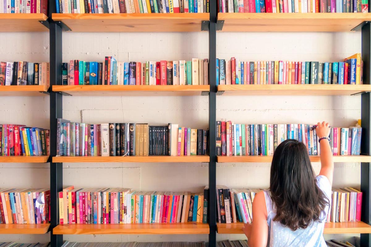 Woman picking up books on a large bookshelf.